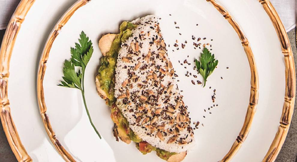Tapioca recheada com frango e guacamole servida em um prato branco decorado com ramos verdes.