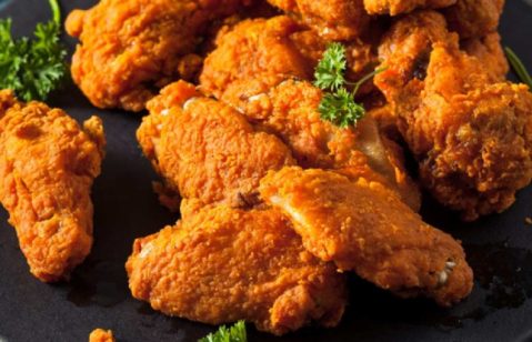 Pedaços de frango frito dispostos em um prato preto liso e raso.