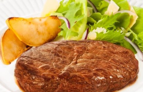Bife de coxão mole servido com salada de folhas faitas de pera e molho de maionese em um prato branco.