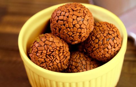 Imagem destaca uma porção de brigadeiro no microondas servido em uma tigela redonda amarela em uma tábua de madeira.