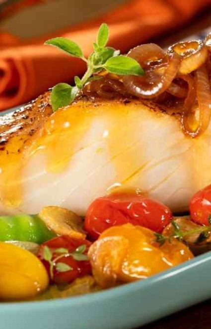 Posta de bacalhau com legumes assados em uma travessa azul claro.