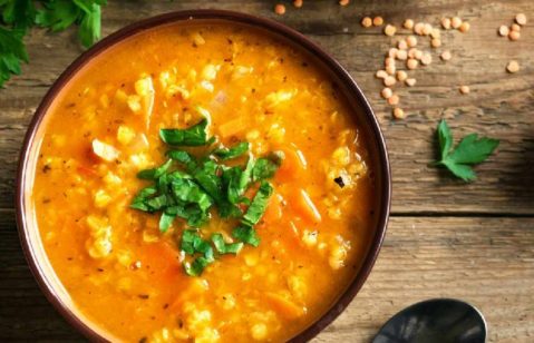 Tigela de sopa de cor amarela servir com cebolinha em uma tigela marrom, em uma mesa de madeira