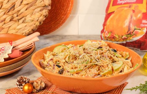 Salada de macarrão gravatinha servido com cenoura, milho e Levíssimo Seara em uma tigela redonda larga, com as bordas marrom. A tigela está em cima de um guardanapo laranja e branco quadriculado, em cima de um jogo americano feito de material parecido com sisal.