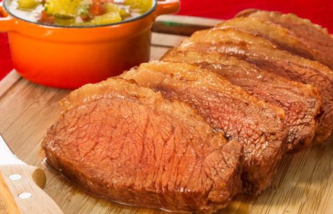 Picanha fatiada em uma tábua de madeira, com uma tigela laranja de vinagrete atrás.