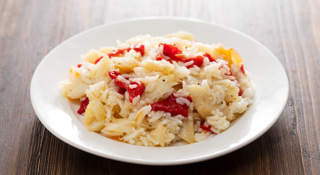Arroz de bacalhau suculento servido em um prato branco fundo e redondo em uma mesa de madeira corrida.