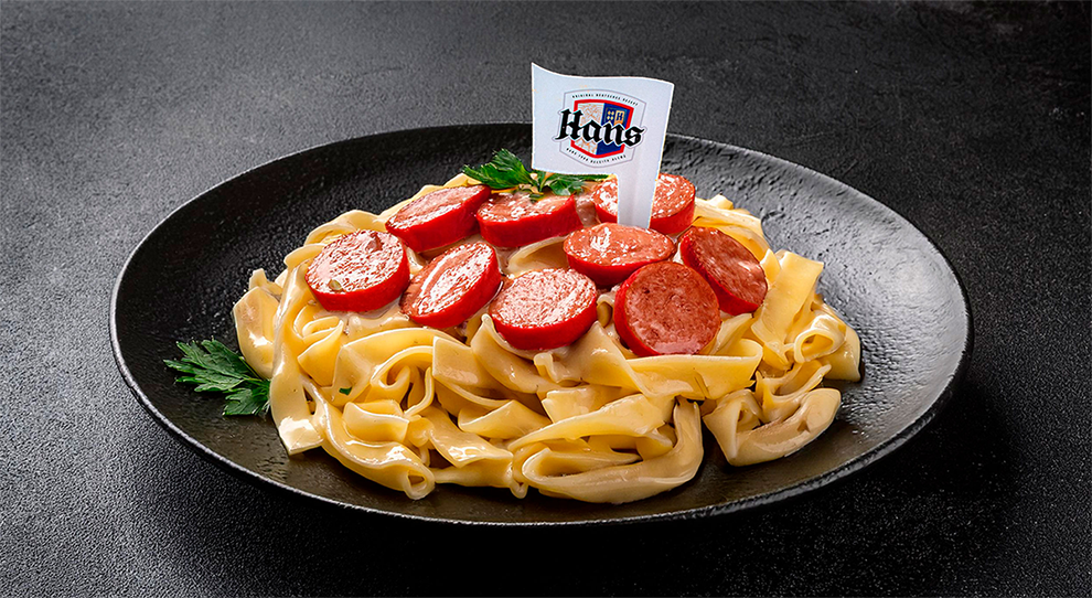 Macarrão cremoso com salsicha de alho em um prato preto sob uma mesa de granito cinza