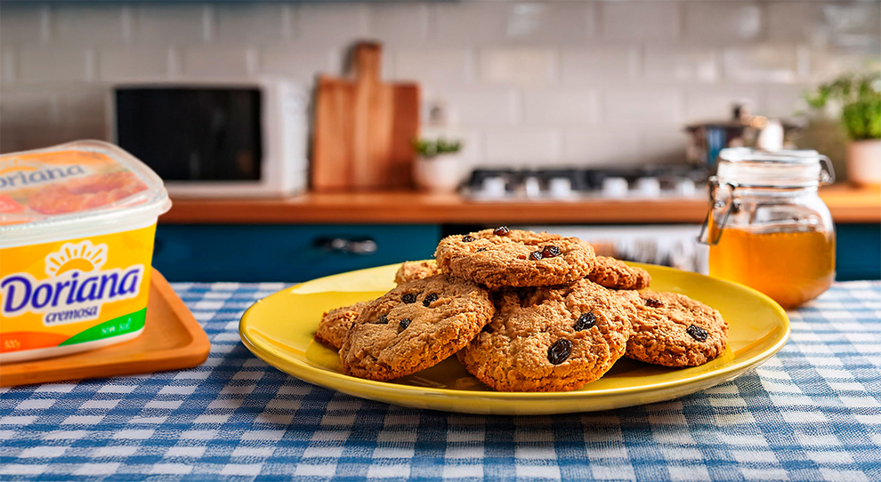 Biscoitos de aveia com gotas de chocolate em destaque, em um prato amarelo sobre uma mesa com toalha xadrez.