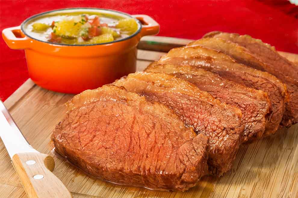 picanha assada em cima de uma tábua de madeira com uma faca ao lado e em cima de uma mesa de madeira