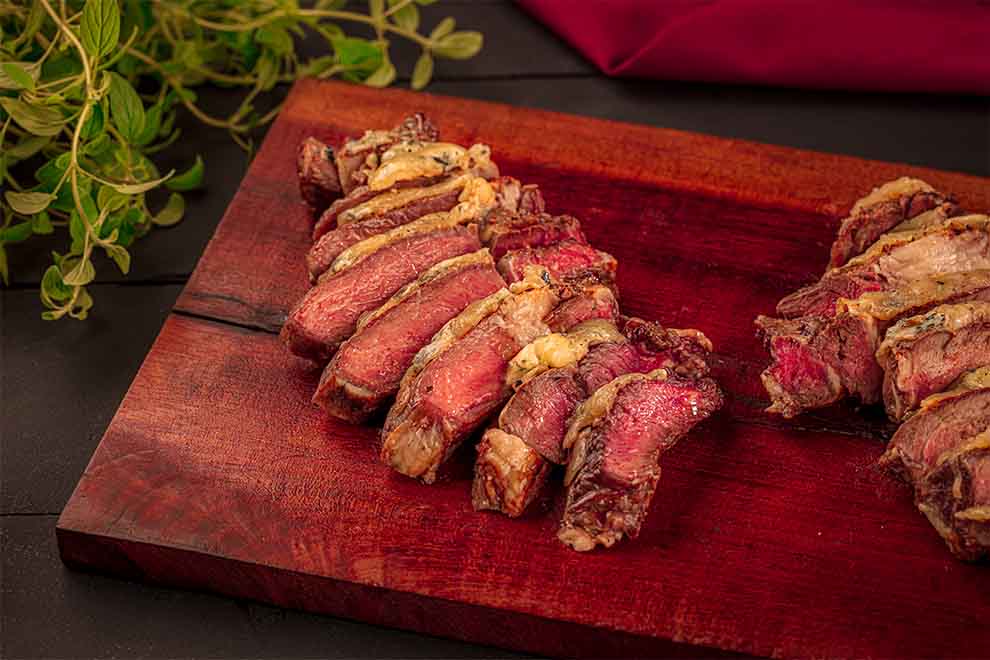 picanha com crosta de gongorzola em cima de uma tábua de madeira e em cima de uma mesa preta.