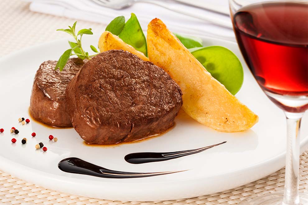 um prato com file mignon e alguns legumes, com uma taça de vinho