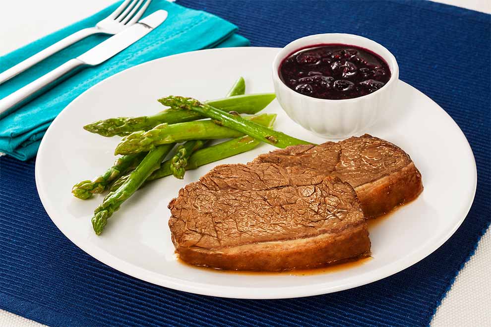 Prato com carne, aspargos e molho de frutas.