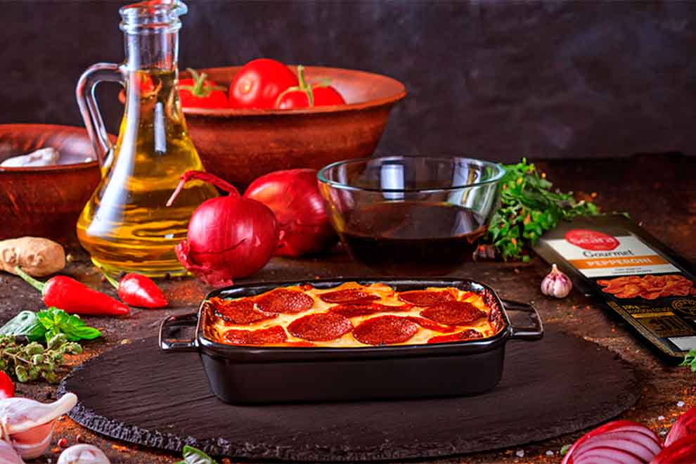Lasanha com pepperoni em mesa de ingredientes frescos