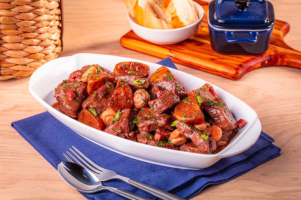 carne de panela com batata dentro de uma travessa branca de porcelana em cima de um guardanapo azul e talheres ao lado