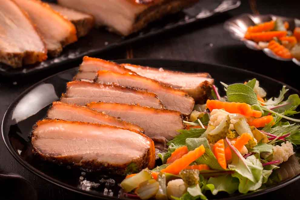 panceta suína com lemon pepper e folhas verdes com picles dentro de um prato fundo preto
