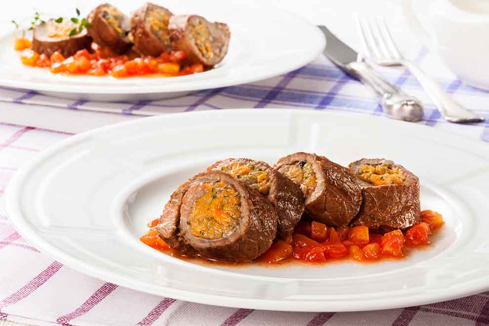 bife de coxão mole recheado dentro de um prato branco redondo de porcelana em cima de um pano xadrez branco e vermelho vinho