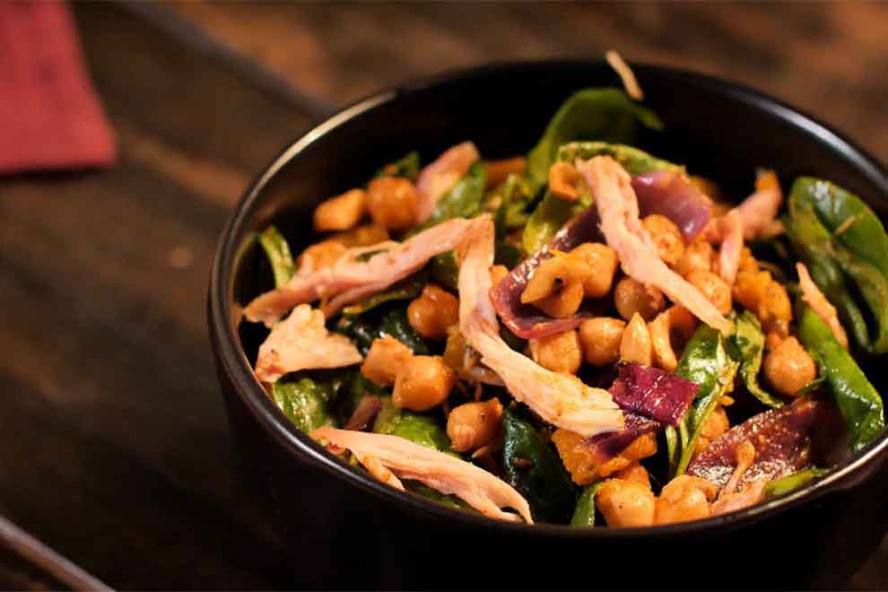 salada de grão de bico com frango defumado dentro de um pequeno bowl de porcelana preta e em cima de uma mesa de madeira escura