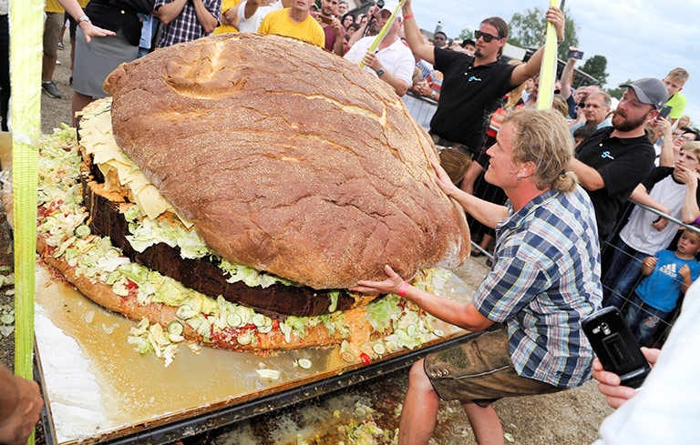 Homem apoiando o maior hambúrguer do mundo, na Alemanha.