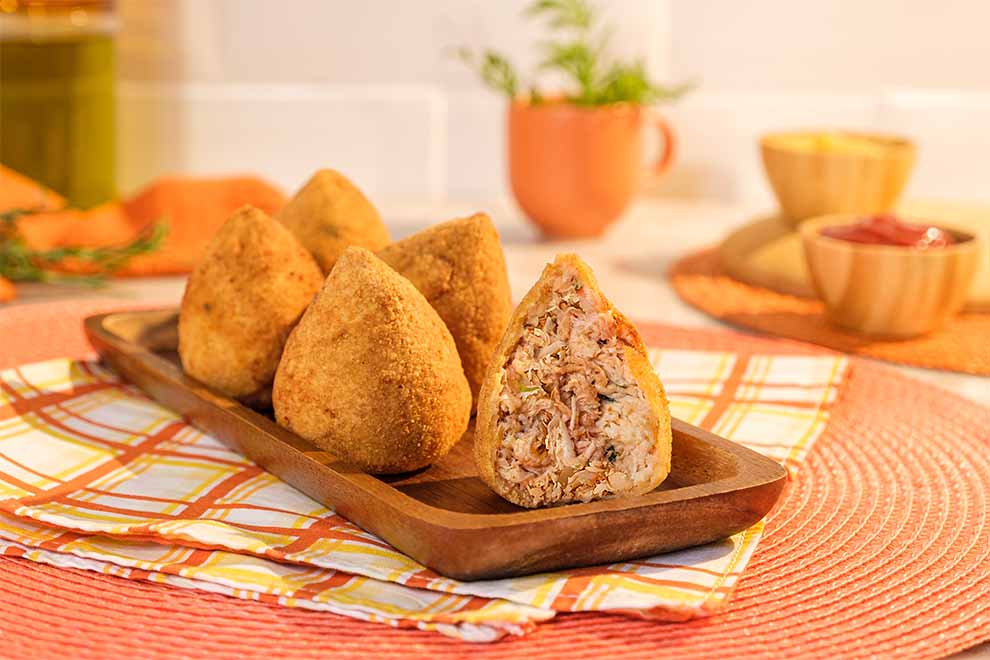 coxinha dentro de um pequeno prato de madeira e em cima de uma mesa com um pano xadrez em branco e laranja