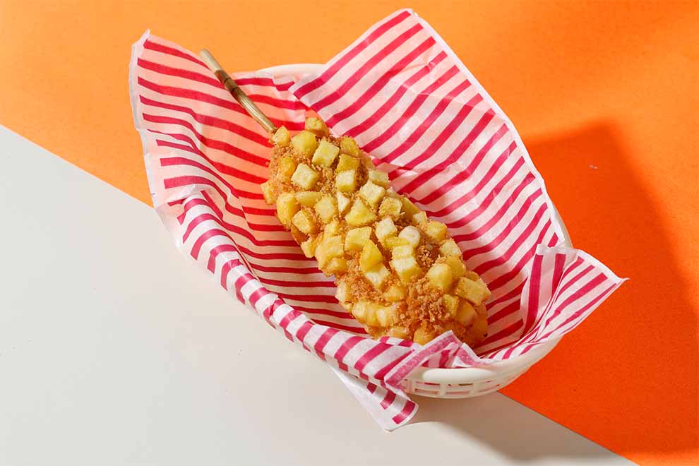 Espetinho de salsicha com batata frita crocante em papel listrado