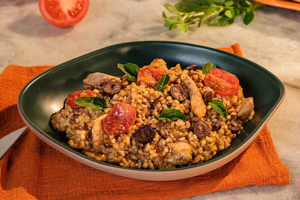 Arroz com frango e tomates, em cima de um prato redondo de cerâmica, sob uma mesa de mármore, com um par de talheres ao lado.