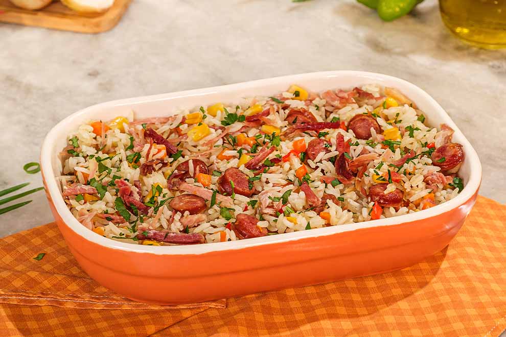 Travessa laranja de cerâmica com Arroz nordestino, sob uma mesa de mármore, com um par de talheres ao lado.