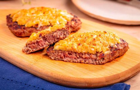 beef burguer com crosta de alho em cima de uma tábua de madeira e em cima de um pano azul escuro e em cima de uma mesa de madeira