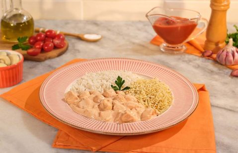 Um prato grande e vermelho com uma porção de enroladinho de salsicha e um pote de molho rosé.